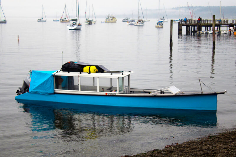 Phil Bolger Idaho sharpie in shoal water near beach.