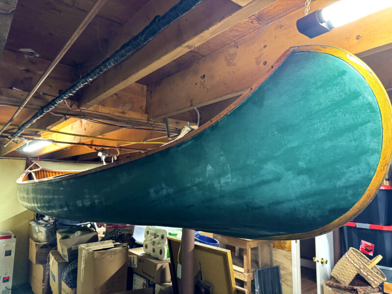 Green wood-and-canvas canoe hanging from basement joists.