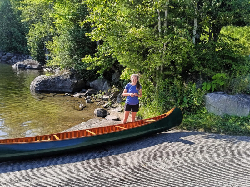 Woman at launching ramp with wood-and-canvas Old Town canoe.