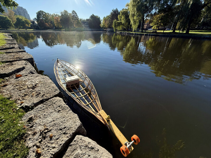 Ultralight see-through kayak in water by stone wall.