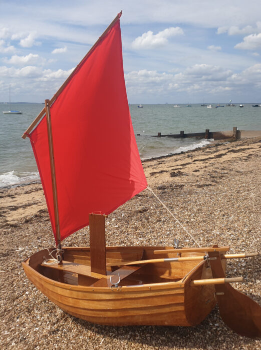 Barrowboat with sail raised on shingle beach.
