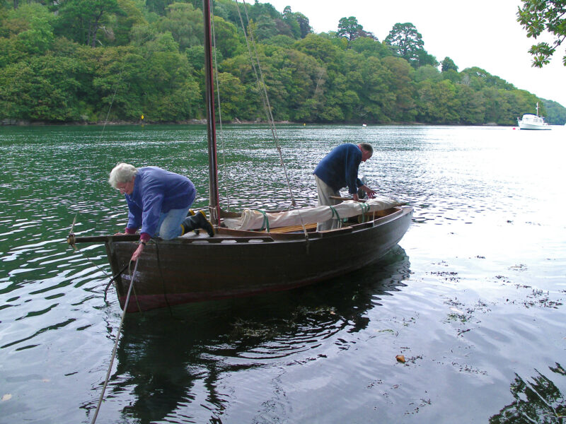 An older couple ready a small wooden boat for sail on the water.