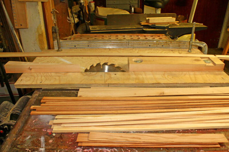 Table saw with infeed and outfeed behind a pile of recently sawn laminate strips.