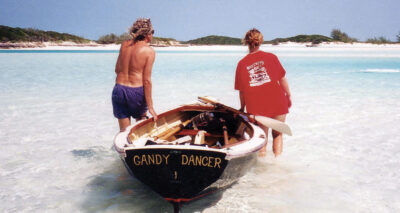 Two paddlers position their rowboat on the water in the Bahamas with an island in the distance.