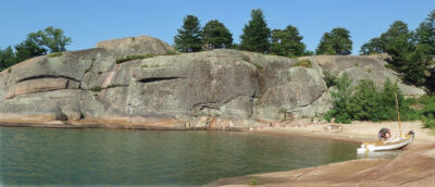 Man tends to gear in his small sailboat on a sandy beach next to a large rockface.