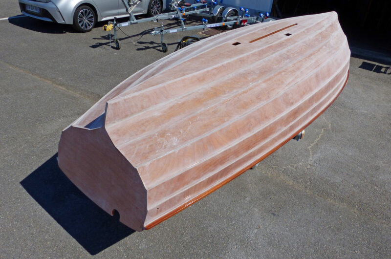 Unfinished wooden hull upside down on paved surface.