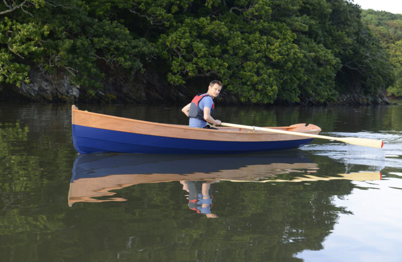 Man rowing a Western Skiff on glassy waters.