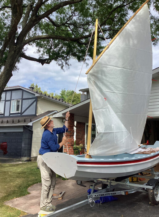 Man raising standing lugsail on painted wooden boat