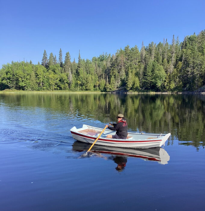 Man rowing painted wooden pram on blue-water lake.