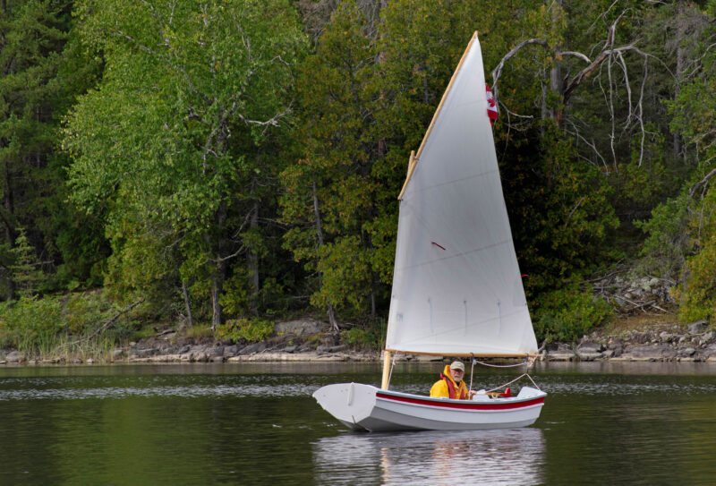 White-painted boat with standing lugsail under way on a calm day.