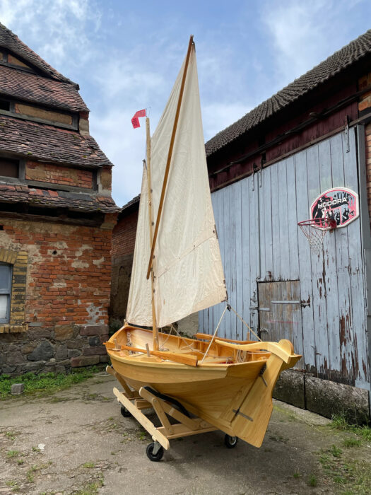 Scandinavian boat, fully rigged, on boat stand in yard.