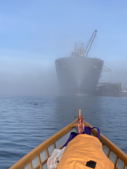 Docked freighter in fog seen over bow of skin-on-frame boat.