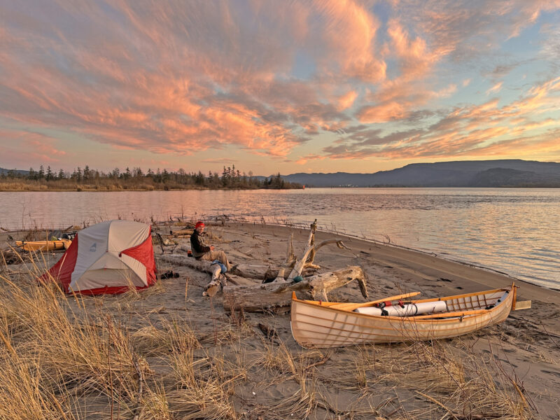 Columbia River campsite with kayak, St Lawrence Skiff, and man at sunset.