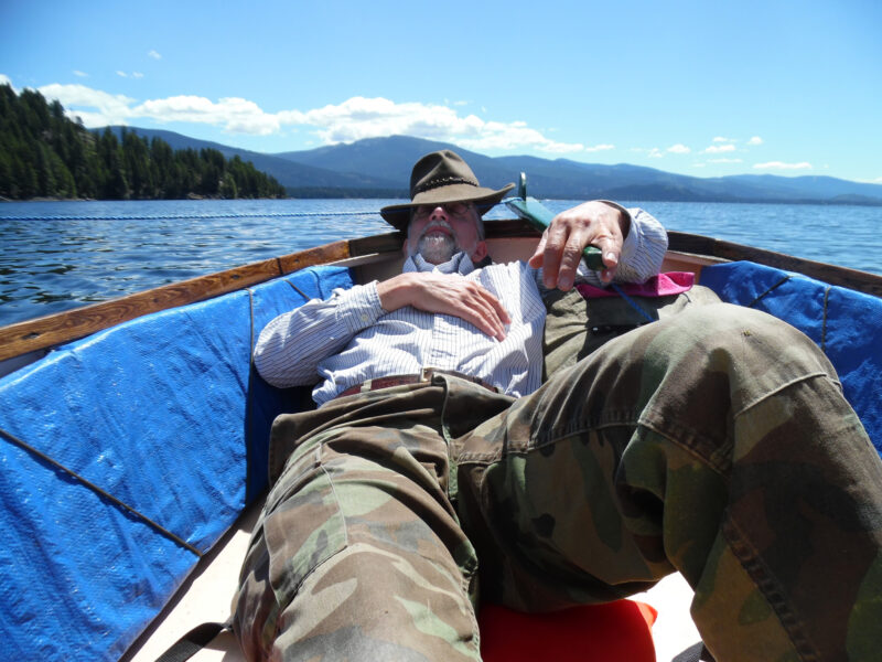 A man reclines at the helm of a small open boat on a sunny day.