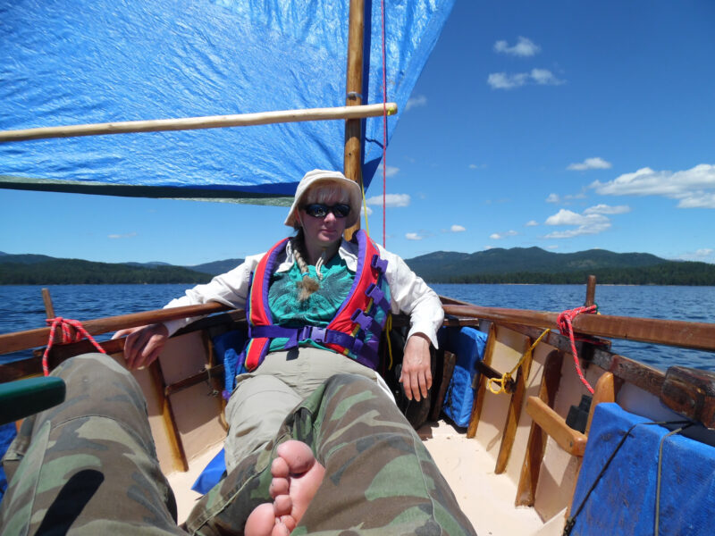 A woman leans against the mast of a small open boat on a sunny day.