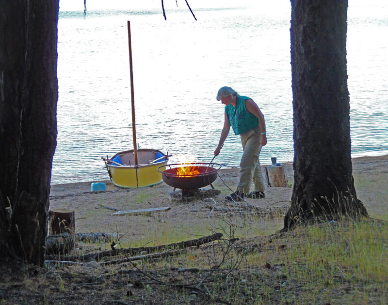 Woman tends a firepit on a sandy beach.