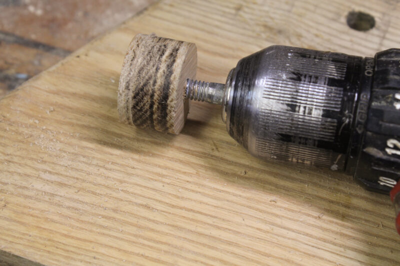Shaping a wooden plug on a hand-held power drill.