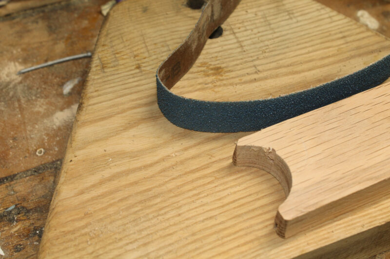 Wood with a half-circle cut out of its end and a sanding belt beside it.