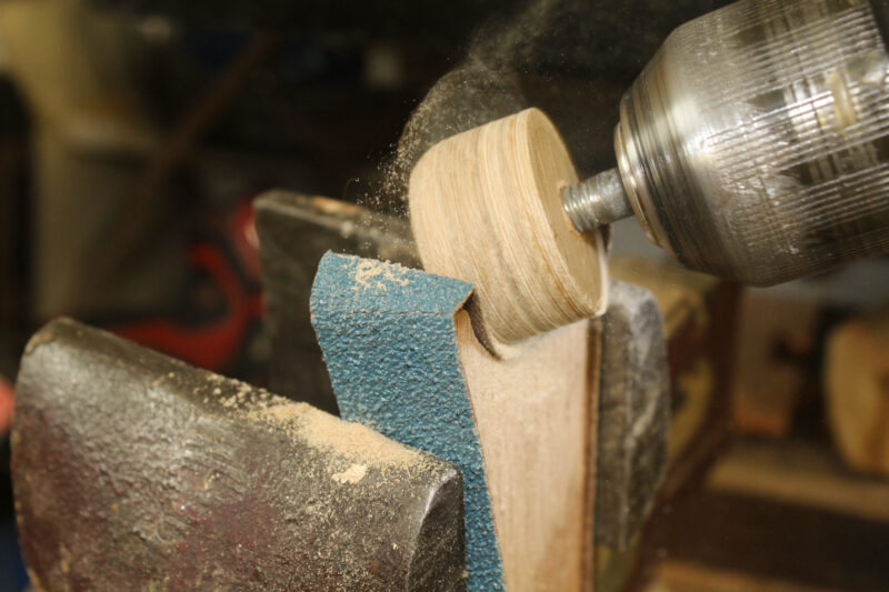 Shaping a wooden plug into a parrel bead with a power drill and sandpaper.