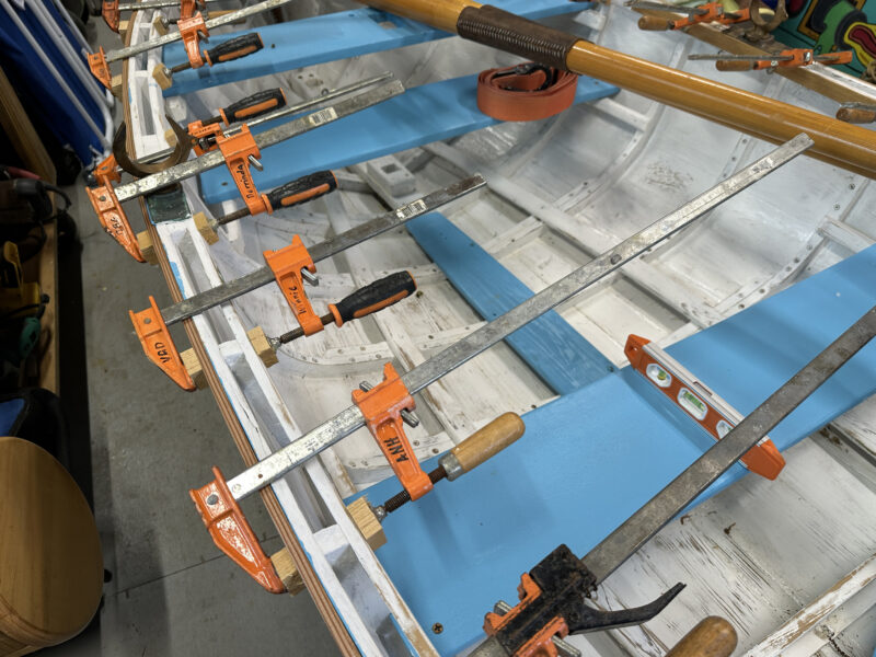 Multiple steel bar clamps being used to hold a new gunwale in place.