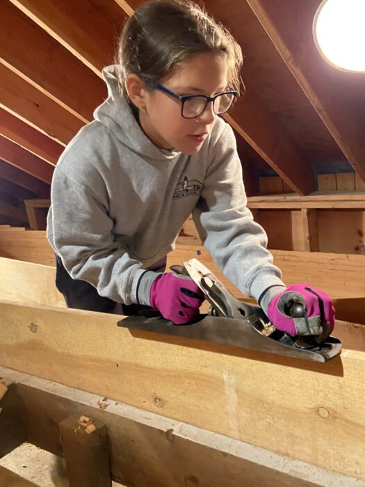 A young girl using a wood plane.