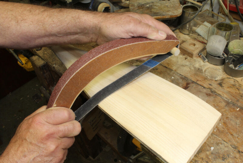 A man uses a sanding bow to shape the blade of an oar.
