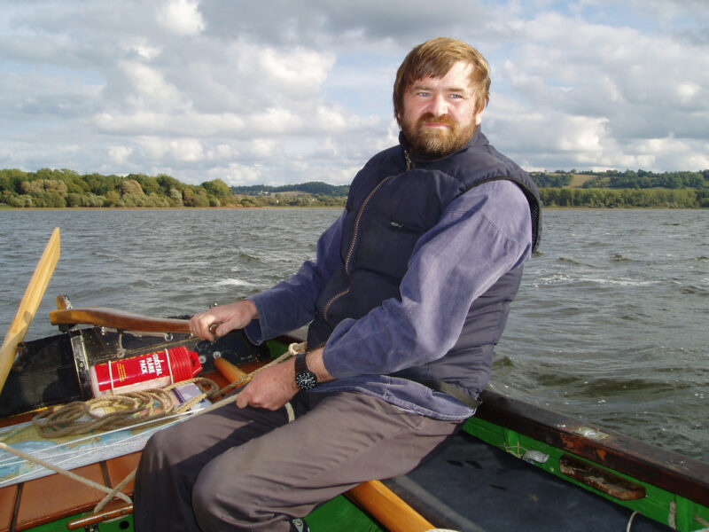 A man helms an open boat off the coast of England.