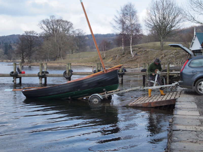 A man winches a lapstrake sailboat up onto a trailer.