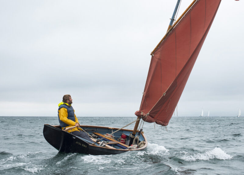 Roger Barnes and AVEL DRO with a fully reefed sail on a grey windy day.