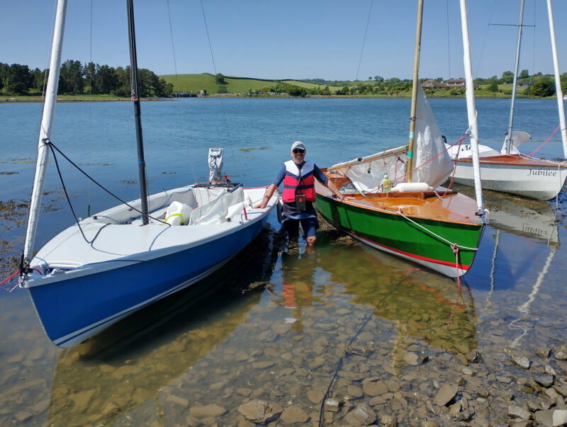 Three Wayfarer sailing dinghies in shallows with man holding on between two.