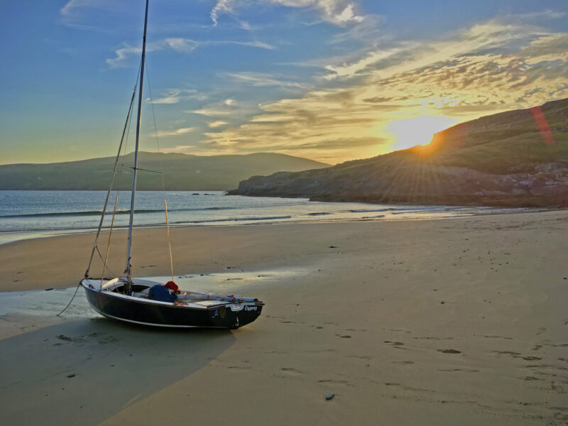 Wayfarer sailing dinghy, high and dry on sandy beach at sunset.