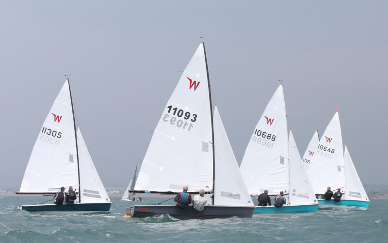 Fleet of racing Wayfarer sailing dinghies going to windward.
