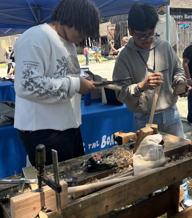 Young men carving miniature wooden paddles.