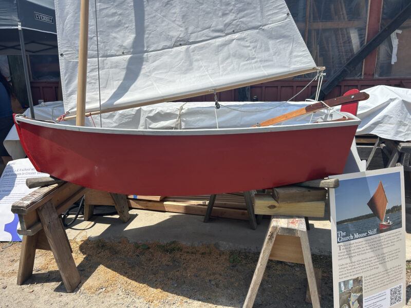 Red-painted skiff with lugsail on saw horses.